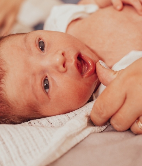 Baby having their lower lip gently pulled down by adult hand