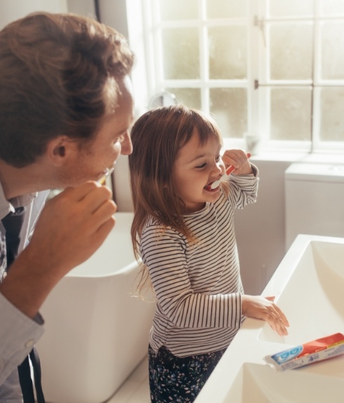 Father and young daughter brushing their teeth together