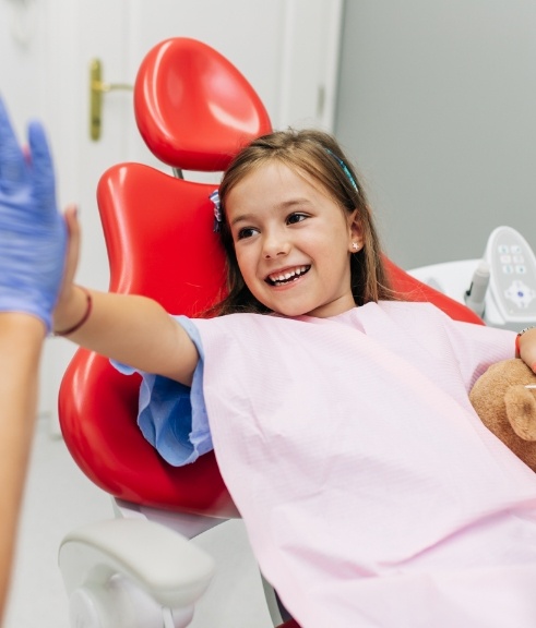 Young girl in dental chair giving high five to her dentist