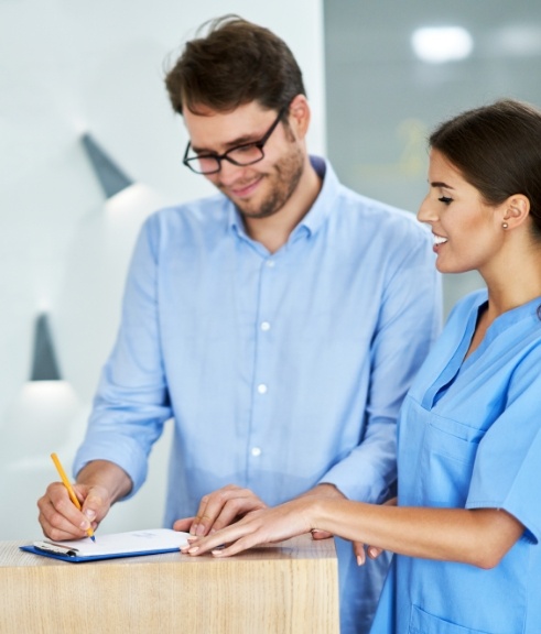 Dental team member showing a patient where to sign on a clipboard