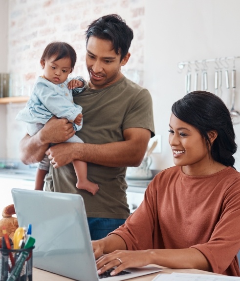 Father holding baby while mother looks at laptop